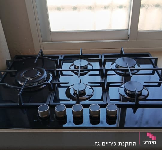 כיריים גז שחורים על משטח מטבח ליד חלון